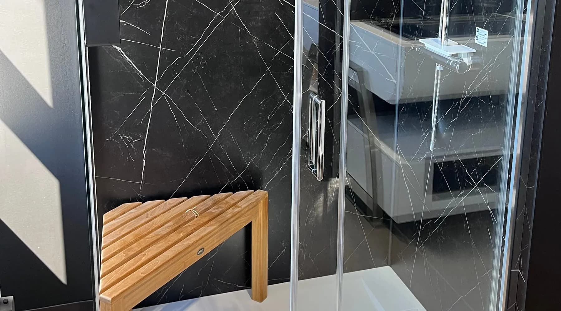 Vitre de douche devant un mur effet marbre noir, avec banc en bois